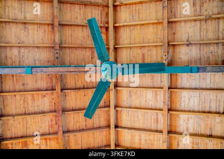 Vista ad angolo basso di un ventilatore a soffitto vintage verde a tre pale contro un soffitto in legno Foto Stock
