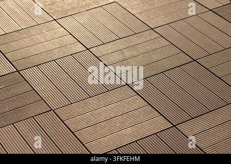 Prima vista di un motivo a piastrelle di legno marrone su un pavimento di terrazza esterno, che mostra assi ruvide, toni caldi e linee geometriche ripetitive come sfondo Foto Stock