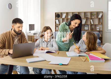 Genitori guidano le figlie nei compiti, la madre spiega mentre il padre è al laptop Foto Stock