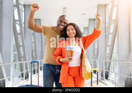 Coppia felice celebra il loro viaggio in aeroporto, alzando le braccia mentre tiene i passaporti Foto Stock