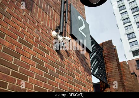 Telecamera di sicurezza installata su muro di mattoni, all'esterno di un edificio urbano, con muro di mattoni, telecamera di sicurezza, cartello numero 2, da una prospettiva ravvicinata Foto Stock