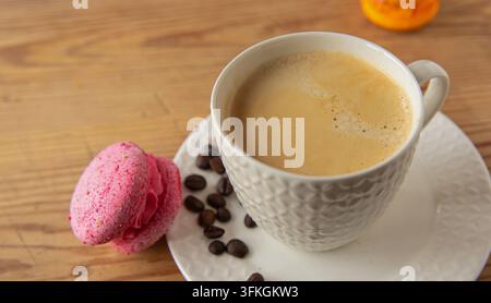 Tazza di caffè con macarons colorati e chicchi di caffè su un tavolo di legno Foto Stock