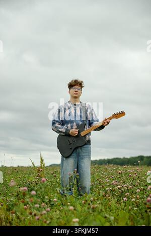 Ritratto di un uomo che suona la chitarra elettrica in un campo di trifoglio all'aperto Foto Stock