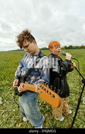Uomo e donna che suonano la chitarra elettrica e cantano in un campo Foto Stock