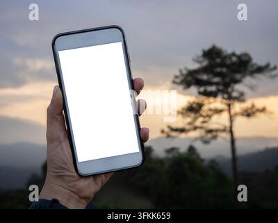 Donna che tiene uno smartphone al tramonto con schermo bianco isolato. Spazio vuoto per il testo. Schermo isolato per modello. Posto di lavoro con spazio per la copia. Foto Stock