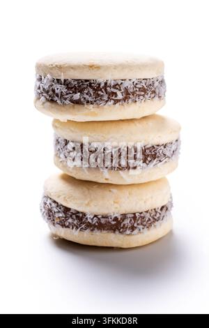 Pila di alfajores tradizionali fatti con biscotti morbidi, ripieni di dulce de leche e ricoperti di cocco grattugiato, isolati su sfondo bianco. Foto Stock
