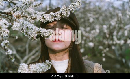 Ritratto ravvicinato di una donna serena con fiori di prugno che sfiorano il suo viso, Moc Chau, Son La, Vietnam Foto Stock
