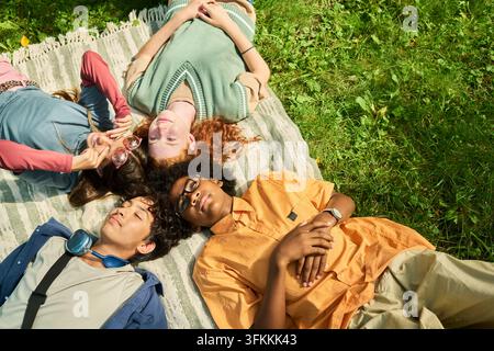 Gruppo diversificato di adolescenti sdraiati su una coperta all'aperto nel parco Foto Stock