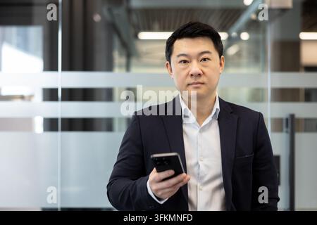 Uomo d'affari che utilizza uno smartphone in un ufficio moderno, uomo professionista che tiene un telefono per la comunicazione aziendale, connettività digitale e tecnologia aziendale in un ambiente di lavoro. Foto Stock