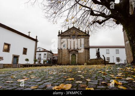 Chiesa storica in pietra nella vecchia città di Braga, Portogallo, circondata da edifici tradizionali portoghesi e alberi autunnali. Foto Stock