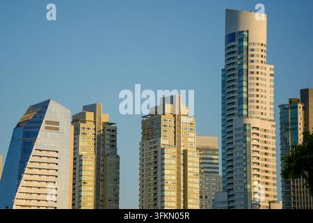 Gruppo di grattacieli residenziali e commerciali moderni immersi in una calda luce dorata contro un cielo blu terso a Buenos Aires. Foto Stock