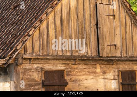 Antica facciata di fienile in legno stagionato con tetto a tegole e persiane Foto Stock
