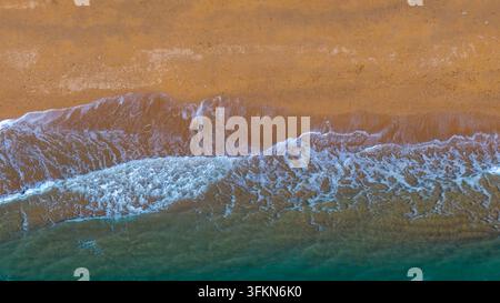Vista aerea della costa con onde gentili che si infrangono sulla sabbia dorata e sull'acqua turchese a West Bay, Inghilterra, Regno Unito. Foto Stock