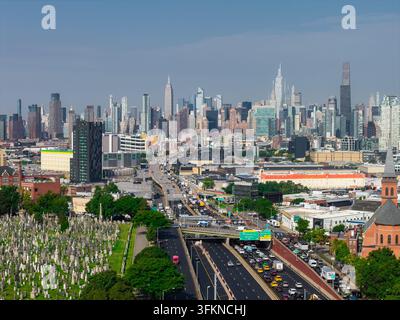 Vista aerea che cattura il traffico lungo la Long Island Expressway a Queens, accanto al Calvary Cemetery, di fronte all'iconica skyline di Midtown Manhattan i Foto Stock