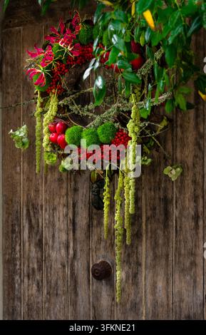 Ghirlanda autunnale rustica realizzata con bacche rosse, fogliame verde, elementi botanici essiccati e rami naturali, esposta su una porta tradizionale in legno Foto Stock