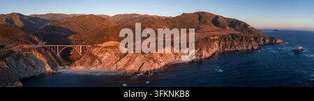 La prospettiva aerea mostra il ponte di Bixby Creek lungo le scogliere frastagliate di Big Sur in California al tramonto. La Highway 1 si estende sul canyon costiero ripido a Foto Stock