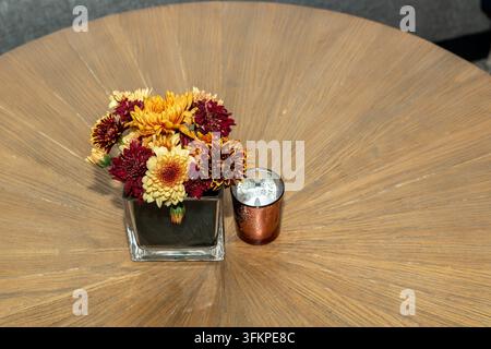 Tavolo di legno decorato con un piccolo mazzo di fiori arancioni e una candela, atmosfera accogliente per la cena, decorazione autunnale calda e concetto di interni naturali Foto Stock
