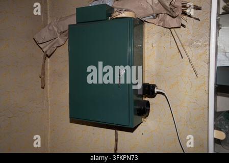 Vecchio armadio elettrico in metallo verde con una chiave, cablaggio, presa di corrente e cavi esposti montati su una parete a motivi. Foto Stock