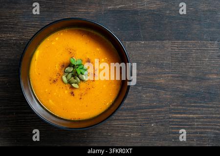 Zuppa di zucca cremosa con semi e prezzemolo, primo piano. Zuppa di zucca arancione vellutata servita in ciotola nera guarnita con semi di zucca e prezzemolo fresco o Foto Stock