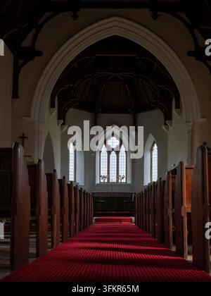 20 settembre 2026, Loweswater, Regno Unito. La luce del sole filtra attraverso le finestre ad arco di una chiesa storica, illuminando il tappeto rosso che conduce Foto Stock