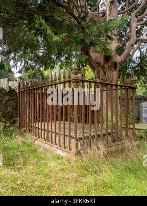 20 settembre 2026, Loweswater, Regno Unito. Una vecchia recinzione in ferro battuto ornata circonda una lapide consumata sotto i rami estesi di un Foto Stock