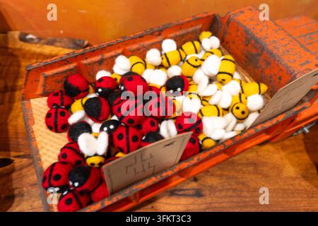 Giocattoli in feltro colorati fatti a mano disposti all'interno di una cassa di legno consumata: coccinelle rosse e nere con api a strisce gialle, texture morbida in tessuto per scaffali per bambini Foto Stock