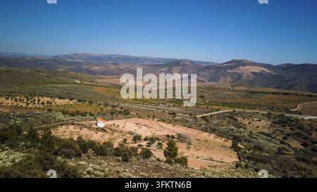 Una vista aerea panoramica cattura il vasto paesaggio aspro e le colline ondulate che circondano Vila Nova de Foz Coa in Portogallo sotto un cielo blu terso. Foto Stock