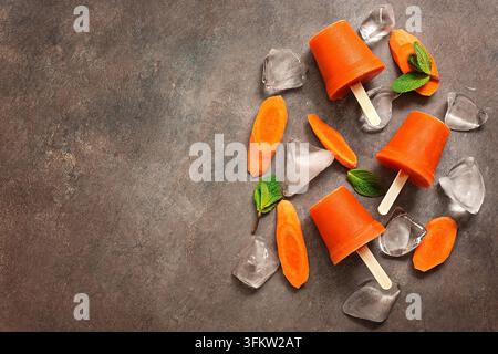 Sano dessert vegano estivo. Gelati. Succo di carota congelato su bastone, sfondo marrone scuro. Vista dall'alto, disposizione piatta, spazio di copia Foto Stock