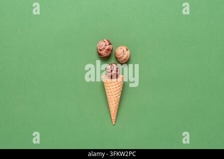 Conchiglie in un cono di waffle per il gelato. Disposizione creativa. Sfondo in carta pastello verde oliva. Vista dall'alto, flat lay. Concetto estivo. Foto Stock