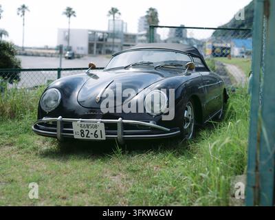 Porsche 356 nero classico parcheggiato sull'erba costiera con palme ad Aichi, Giappone Foto Stock