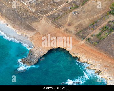Vista aerea della Riserva Naturale Orientata dello Zingaro con una piccola auto arancione parcheggiata su un sentiero sterrato vicino alle acque turchesi e alla costa rocciosa Foto Stock