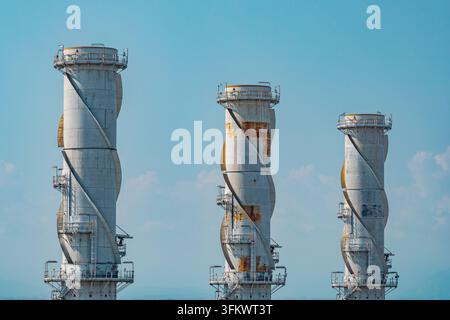 Vista aerea di tre distintive ciminiere di scarico che si ergono sopra una moderna centrale a ciclo combinato sotto un cielo blu terso a Chivasso, Piemonte, Italia. Foto Stock