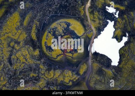 Vista aerea di un cratere vulcanico circondato da campi di lava ricoperti di muschio verde vibrante e chiazze di neve bianca nelle terre alte islandesi, Islanda. Foto Stock