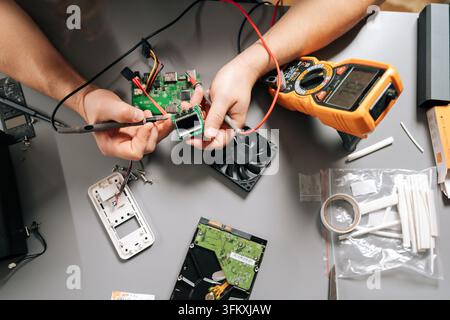 Primo piano di un tecnico che utilizza un multimetro per diagnosticare una scheda elettronica, risolvere problemi di hardware informatico, installare componenti e riparare attrezzature moderne Foto Stock