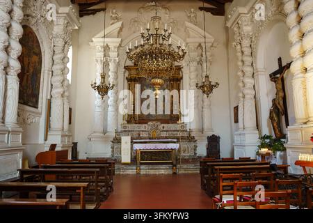 Taormina, Italia – 26 giugno 2026: La Chiesa di Santa Caterina d’Alessandria, interno di una chiesa barocca tradizionale con colonne bianche ornate, un altare dorato, lampadari appesi e file di panche di legno Foto Stock