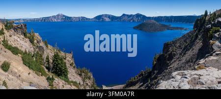 Vista del lago vulcanico blu profondo di Crater Lake in Oregon da Merriam Point che mostra rive rocciose ripide e montagne lontane Foto Stock