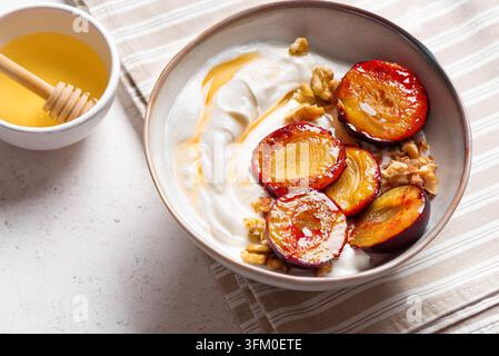 Prugne arrosto con yogurt, miele e noci. Ciotola di colazione sana o dessert - prugne grigliate e yogurt greco con granola di noci fatta in casa. Foto Stock