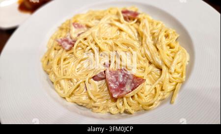 Spaghetti carbonara cremoso con pancetta in una ricca salsa al formaggio, servito su un piatto bianco in un ristorante. Foto Stock