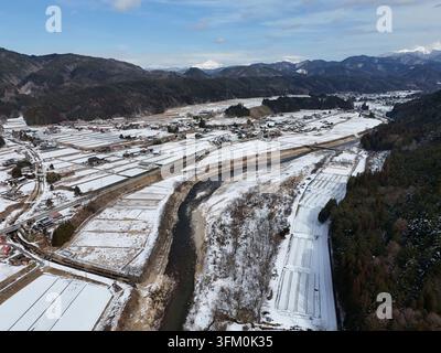 Un paesaggio innevato con un fiume che lo attraversa. Il fiume è circondato dalla neve e le montagne sullo sfondo. La scena e' tranquilla e serena Foto Stock