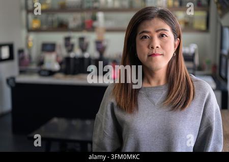 La donna transgender thailandese del sud-est asiatico, con i suoi 40 anni, sta in casa mentre è a diretto contatto visivo con la fotocamera. Mantiene un viso calmo e neutrale Foto Stock