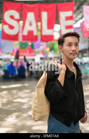 Un ritratto verticale medio di un gay non binario di Isan, di origine thailandese all'aperto in un corridoio del mercato di strada. Il modello ha poco buio Foto Stock