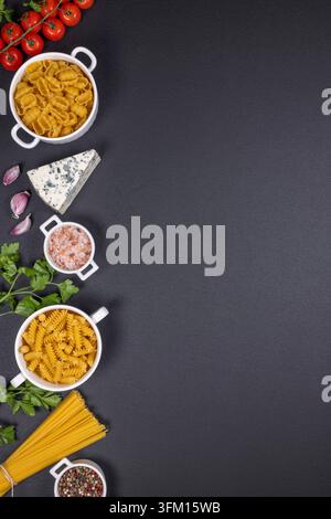 Pasta italiana cruda assortita - fusilli, gnocchi, spaghetti - in ciotole bianche con pomodori, aglio, prezzemolo, gorgonzola, sale e pepe su una superficie scura texture Foto Stock