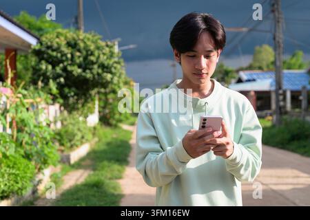 Un ritratto orizzontale dello stile di vita di un bel giovane asiatico della regione di Isan in Thailandia, in una strada rurale di un villaggio. Guarda in basso con lui Foto Stock