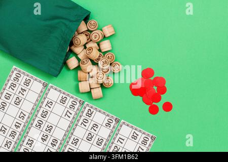 Barili di lotto in legno con sacchetto di stoffa, carte da gioco e fiches rosse su sfondo verde. Gioco da tavolo lotteria. Vista dall'alto con spazio per il testo Foto Stock