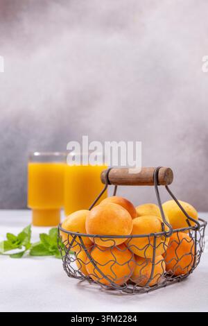 Albicocche in un cesto di metallo rustico poggiate su una superficie chiara con due bicchieri di succo appena spremuto e foglie di menta sullo sfondo, rappresentanti la salute Foto Stock