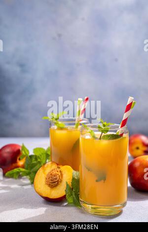 Due bicchieri di succo di nettarina fatto in casa con menta fresca, ghiaccio e cannuccia a strisce, con nettarine intere e a metà su una superficie rustica, creando un Foto Stock