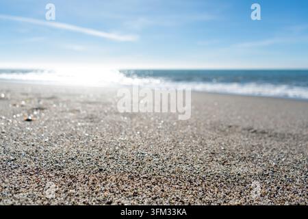 Questa tranquilla scena di spiaggia cattura la bellezza scintillante della sabbia bagnata sotto un cielo luminoso e sereno. Le onde gentili si infrangono sulla riva, creando un effetto ipnotico Foto Stock