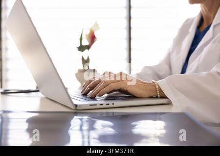 Primo piano di una dottoressa che lavora online utilizzando un laptop alla scrivania della clinica Foto Stock