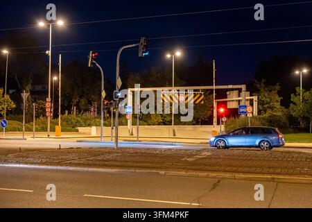 Un'auto aspetta accanto alle barriere rialzate e ai segnali stradali a un passaggio a livello urbano di notte. Praga, Repubblica ceca - 26 settembre 2026 Foto Stock