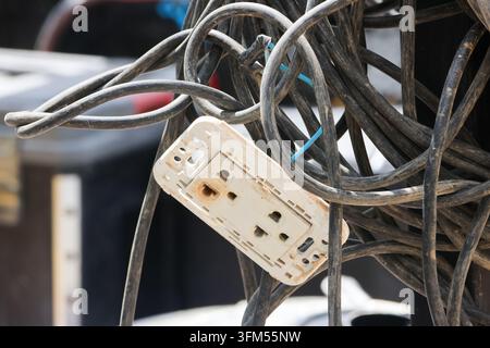 Un cavo ingarbugliato e una presa elettrica danneggiata che creano una scena di manutenzione pericolosa con cablaggi esposti e disordine industriale in un'area di lavoro all'aperto Foto Stock